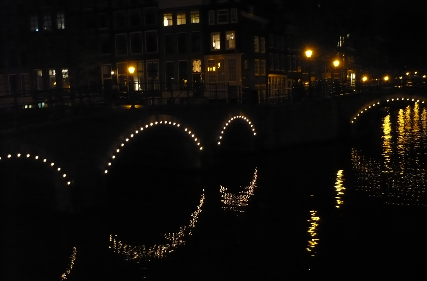 "La imagen captura la atmósfera mágica y vibrante de Ámsterdam. Los emblemáticos canales reflejan la arquitectura única de la ciudad, con casas estrechas y altas que se inclinan ligeramente sobre el agua. Botes y barcazas adornan los canales, añadiendo movimiento y vida a la escena. Los puentes de piedra conectan las orillas, mientras que las flores en los alféizares y jardines aportan un estallido de colores. Es una ciudad donde la historia y la modernidad coexisten en perfecta armonía, donde la cultura y el arte se respiran en cada esquina. Esta imagen es una ventana a la belleza y la singularidad de Ámsterdam, invitando a explorar sus encantos únicos."